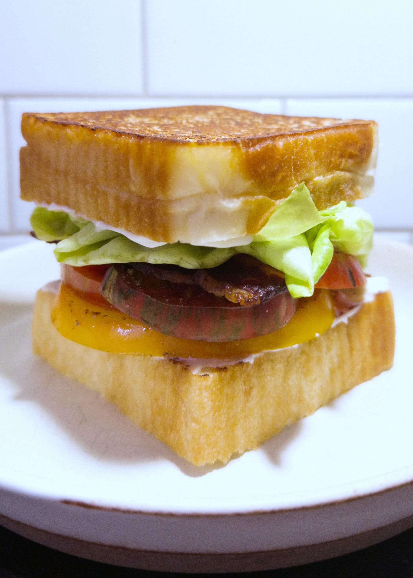 Stacked sandwich of lettuce, multi-coloured tomatoes, bacon, and mayo between slices of thick white bread