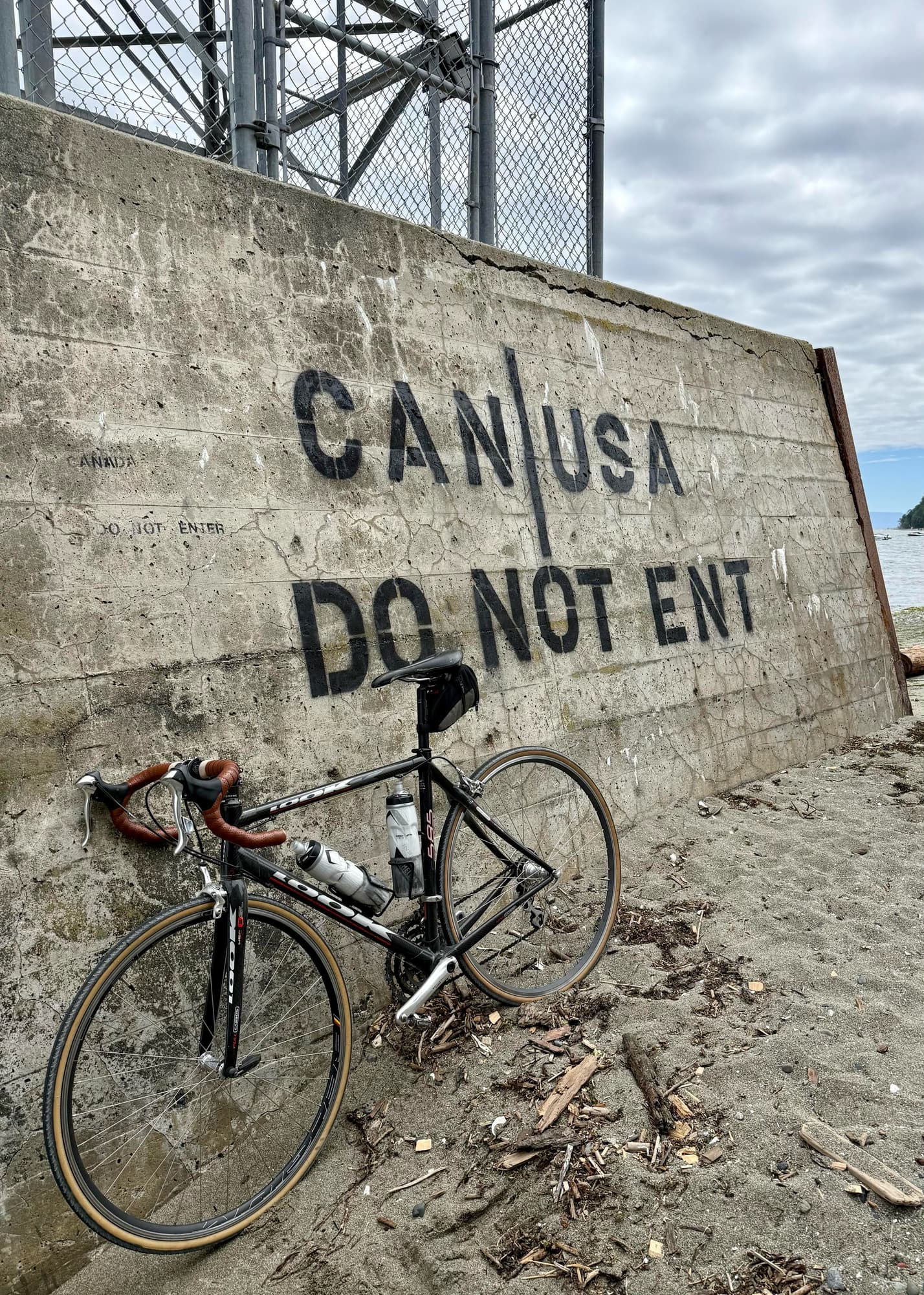 Road bike in front of a concrete pylon on a beach, spray-painted with the words 