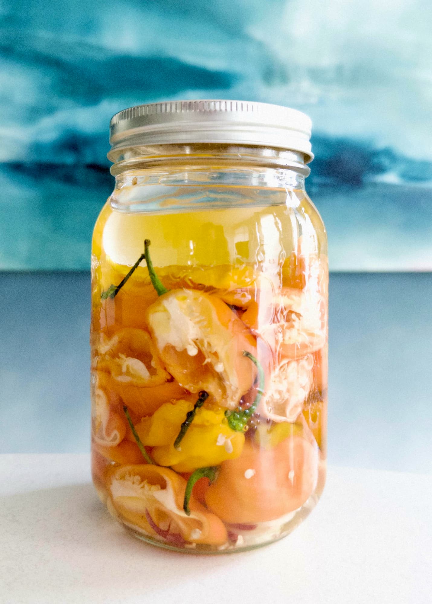 Tall mason jar of yellow and orange peppers in clear liquid