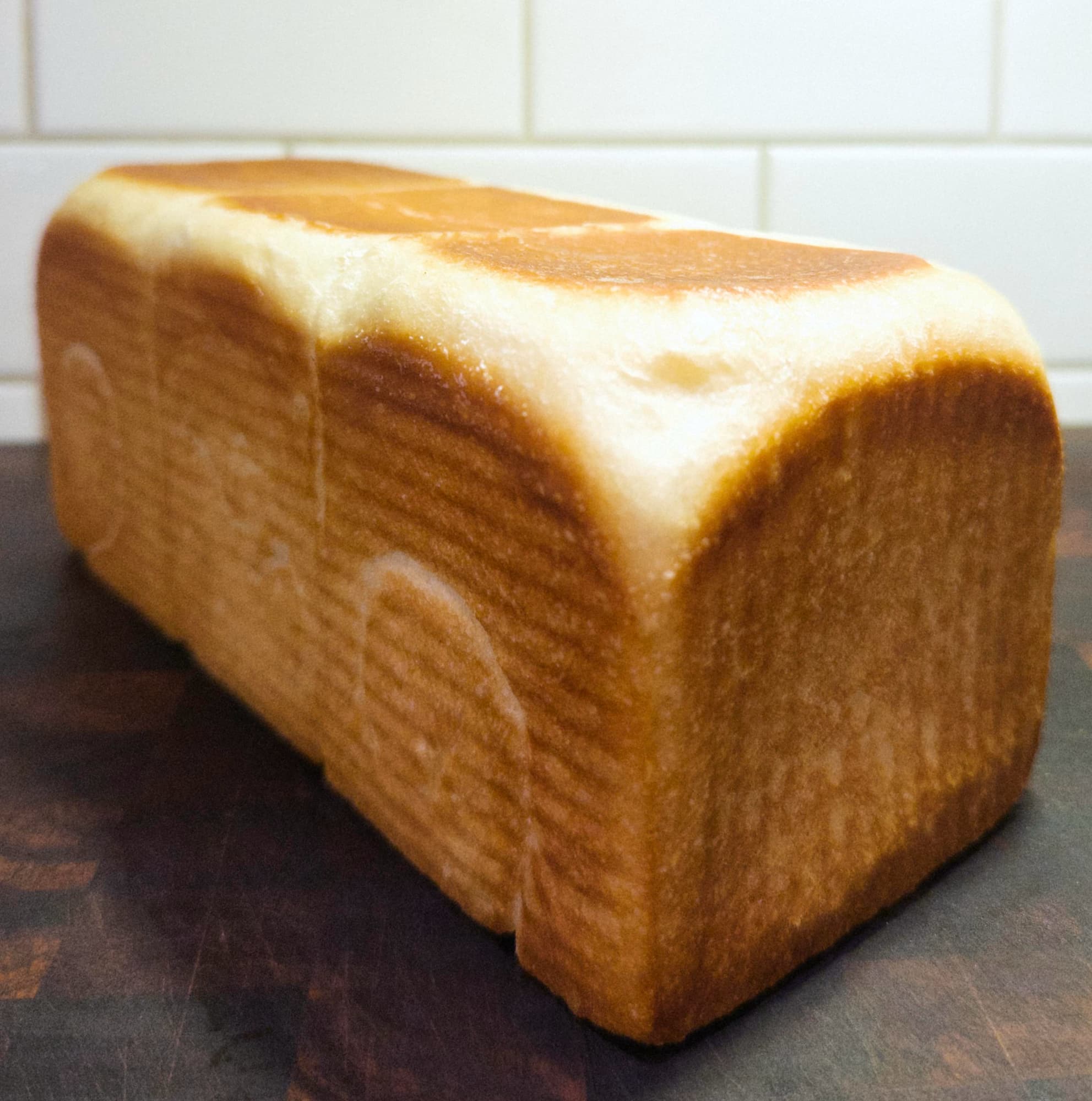 Full loaf of squared-off white bread in three joined cube sections on a wooden cutting board