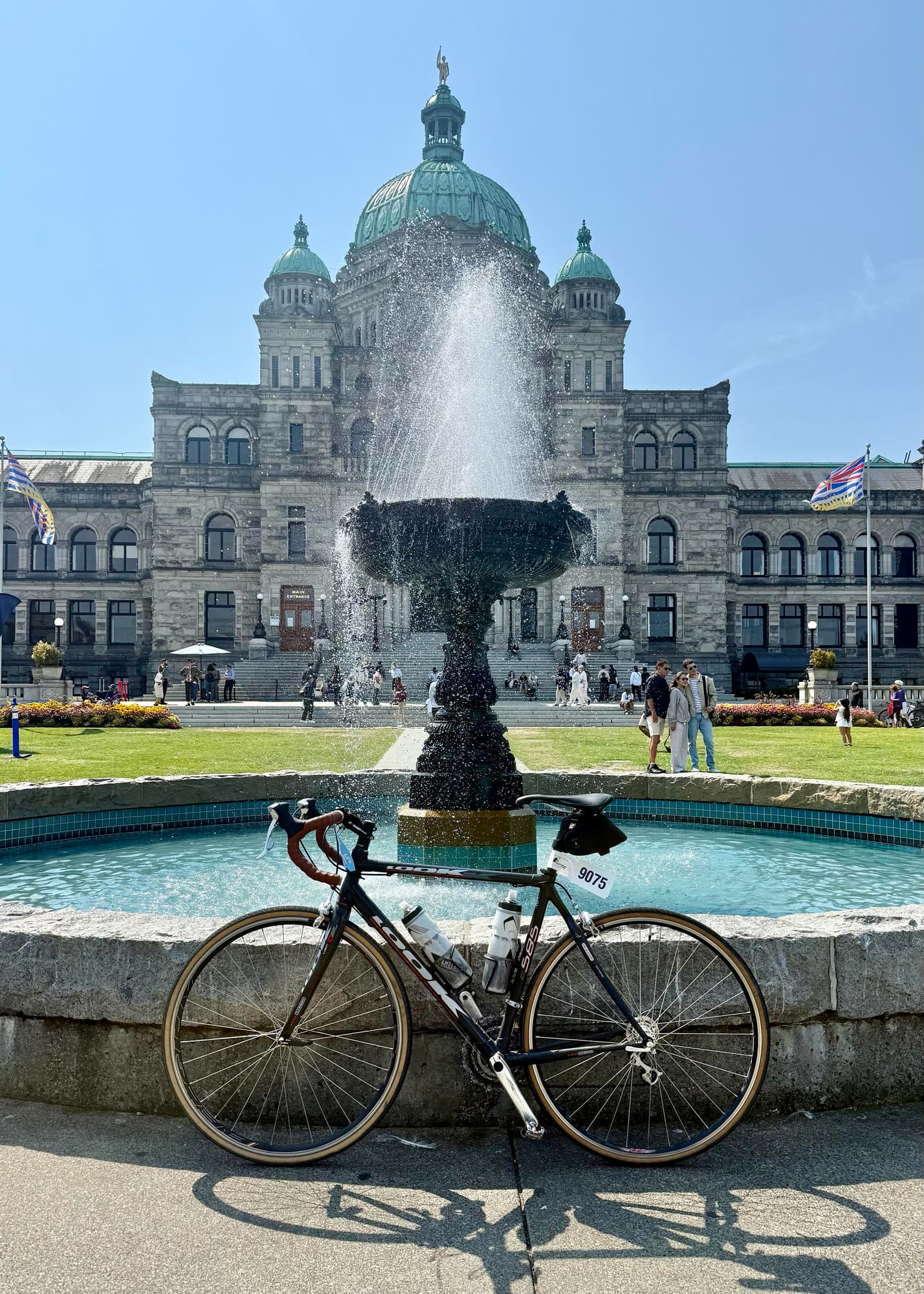 Road bike with a numbered tag of 9075 parked against a fountain in front of BC's legislature buildings