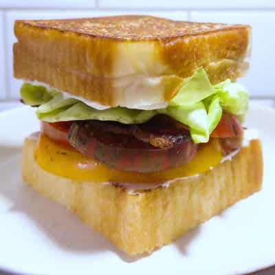 Stacked sandwich of lettuce, multi-coloured tomatoes, bacon, and mayo between slices of thick white bread