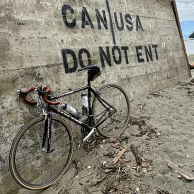 Road bike in front of a concrete pylon on a beach, spray-painted with the words 