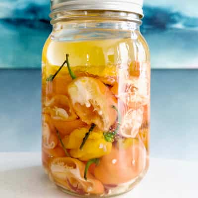 Tall mason jar of yellow and orange peppers in clear liquid
