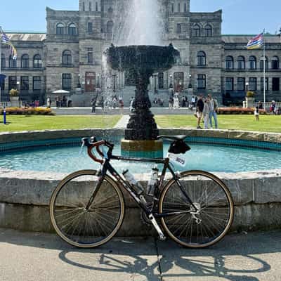 Road bike with a numbered tag of 9075 parked against a fountain in front of BC's legislature buildings
