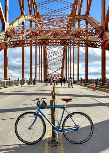 Blue bike parked in the center of a nearly empty bridge with faded orange steel support structure overtop