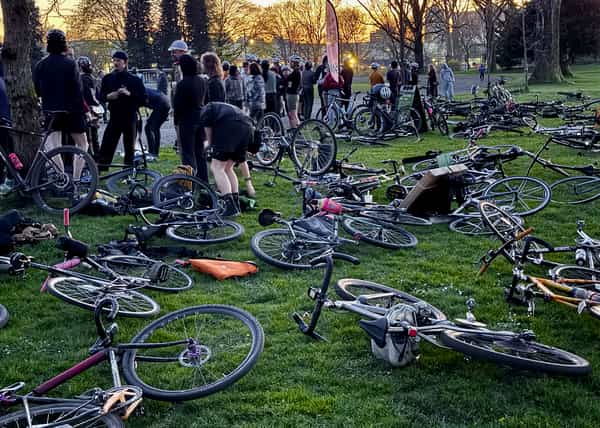 Plenty of bikes in the grass with a crowd facing away watching the action