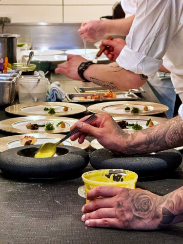 Many hands plating fancy dishes in a line