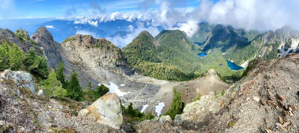Sweeping mountaintop vista from high up overlooking ocean, trees, snow, lakes, and other mountains below