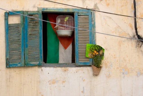 Peeling blue-painted wooden shutters partially open to reveal a birdcage and Jordanian flag