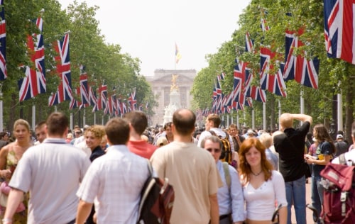 Busy crowd-filled street lined with trees and UK flags