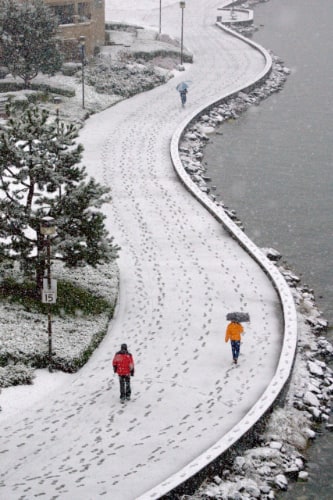 Curved seaside path covered in snow and footprints with three people walking at varying distances
