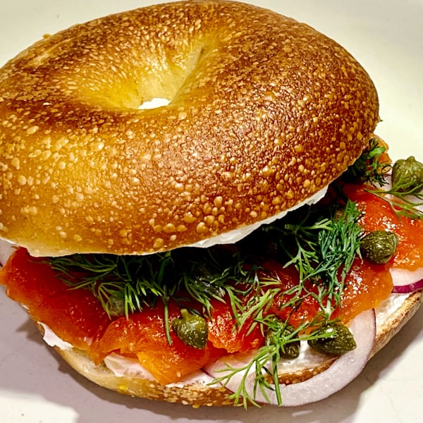 Nicely-blistered bagel halved and filled with cream cheese, lox, dill, capers, and onion