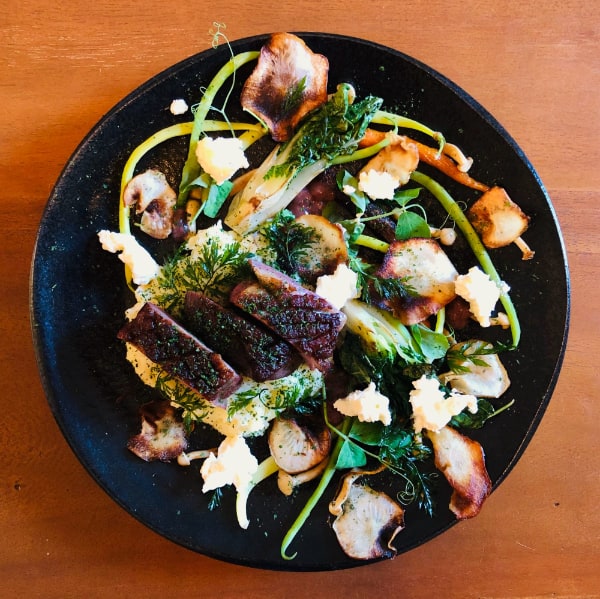 Three thick slices of duck breast with well-crisped skin on a white puree surrounded by long green beans, crispy chips, mushrooms and herbs