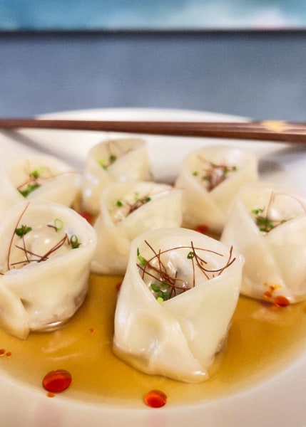 Folded dumplings standing upright in a clear broth dotted with red oil