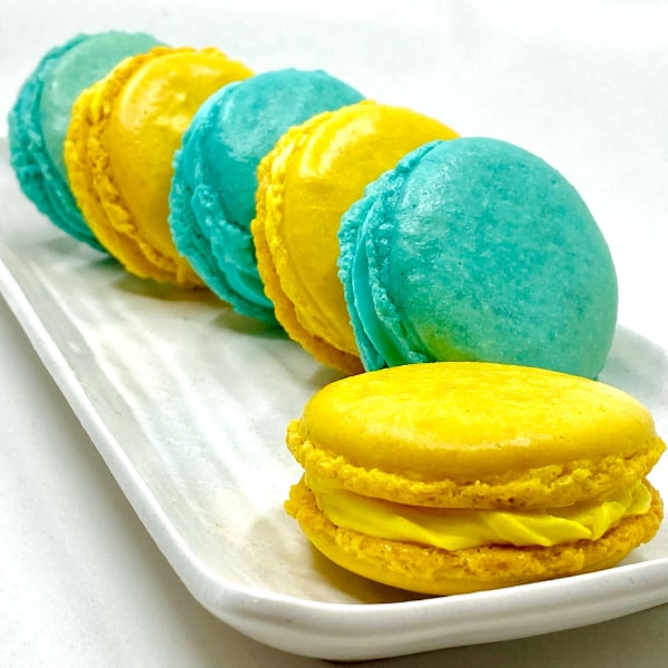 Rectangular white dish with alternating teal and canary yellow macarons arranged