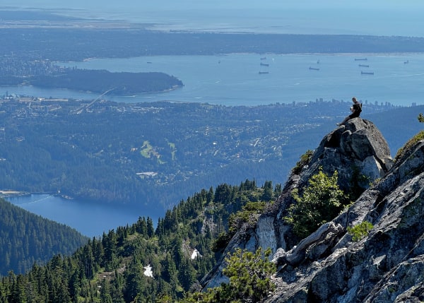Solitary figure sitting on a rock outcropping overlooking the city of Vancouver far below