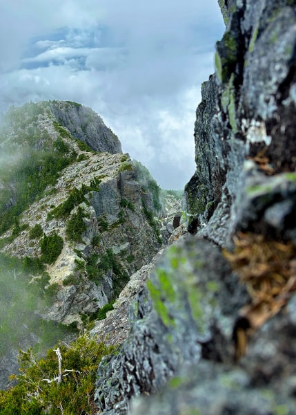 Blurred rocks in the extreme foreground, mountain ridge and cloud below