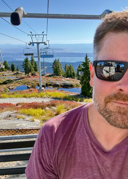 Self-portrait in sunglasses while seated on a chairlift that runs down the mountain behind