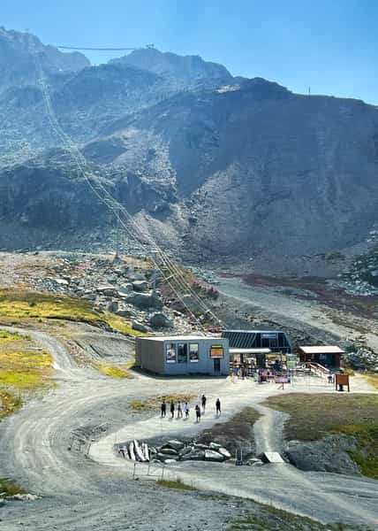 Gravel paths leading to a chairlift base that runs up jagged rocky cliffs behind on a gorgeous sunny day
