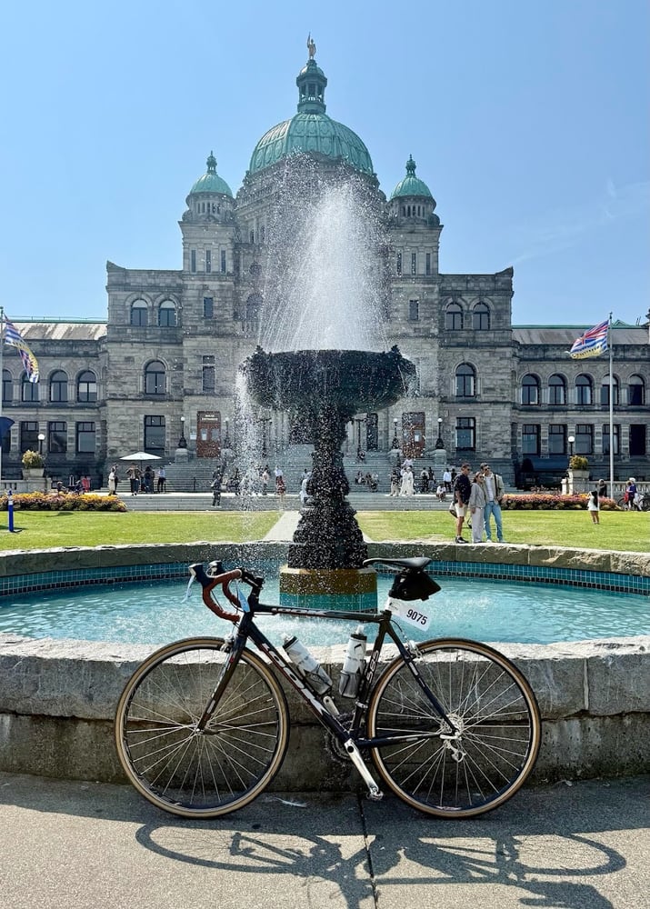 Road bike with a numbered tag of 9075 parked against a fountain in front of BC's legislature buildings