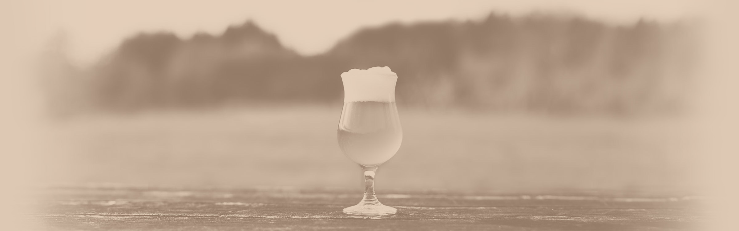 Brown-toned photo of a tulip glass on a wooden surface filled with a foamy liquid