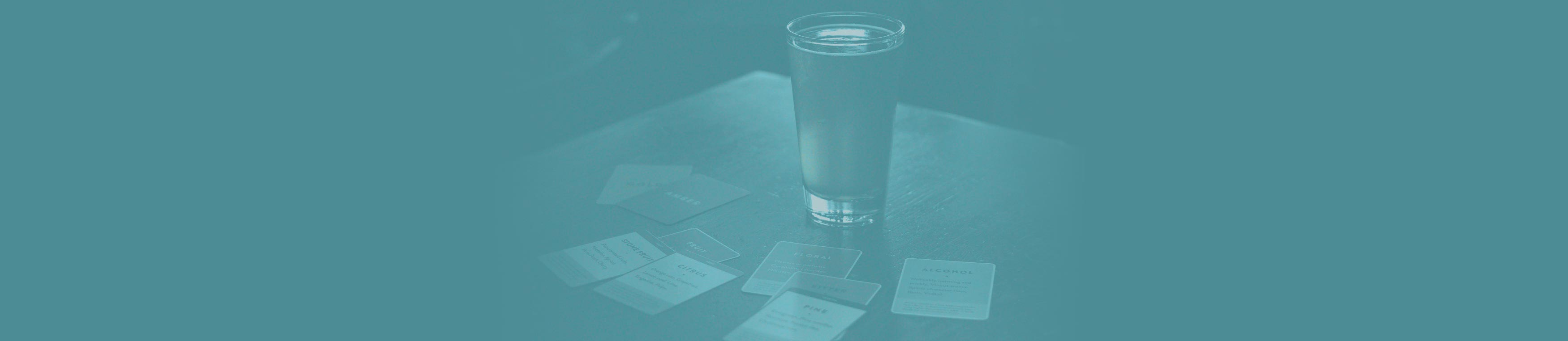 Blue-toned photo of a full pint glass surrounded by fanned-out playing cards