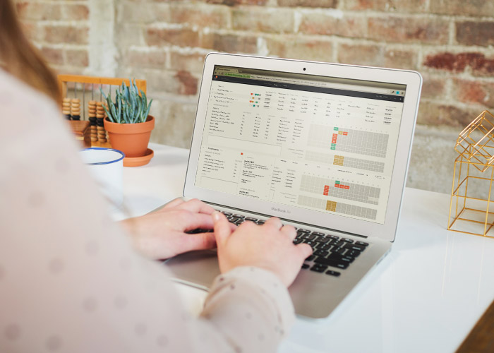 Looking over a woman's shoulder at a fancy desk, hands poised over the keyboard of a Macbook with the client tracker on screen.
